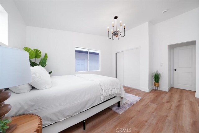 bedroom with light wood-style flooring, a chandelier, a closet, and baseboards