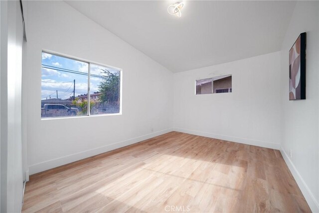 spare room featuring lofted ceiling, light wood-type flooring, and baseboards