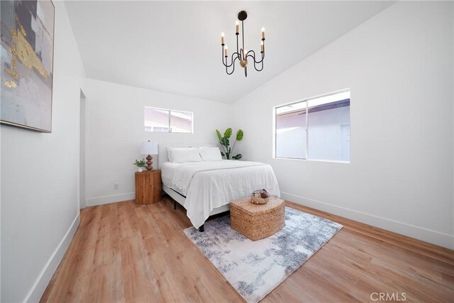 bedroom featuring baseboards, a chandelier, light wood-style flooring, and vaulted ceiling