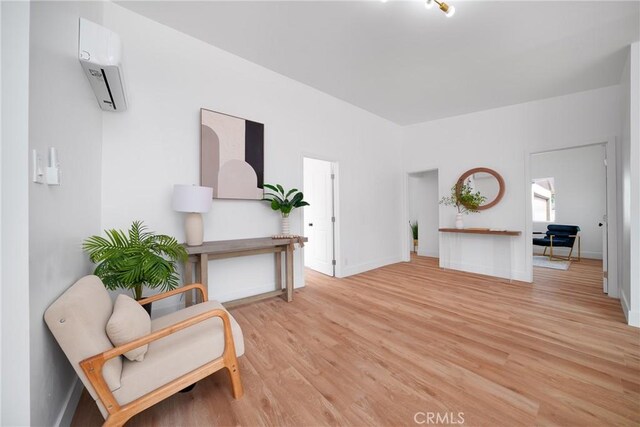 living area featuring light wood-style floors, baseboards, and a wall mounted AC