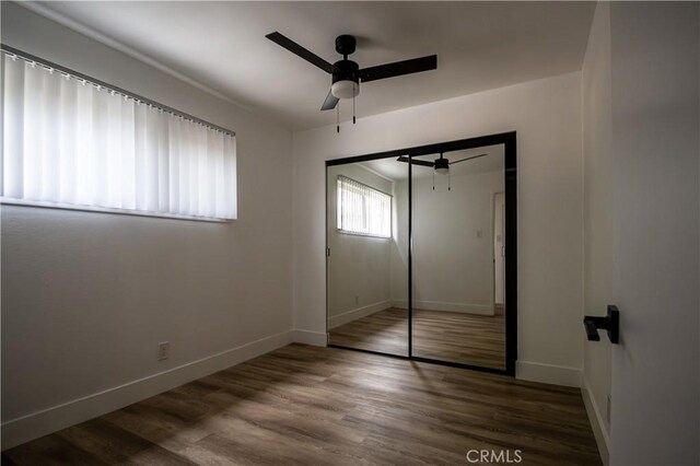 unfurnished bedroom with baseboards, wood finished floors, a closet, and ceiling fan