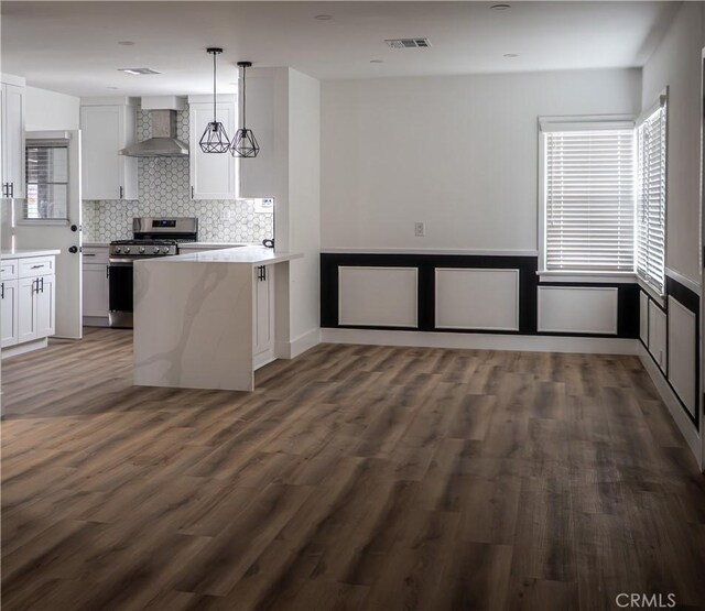 kitchen with stainless steel gas range, wall chimney exhaust hood, white cabinets, a peninsula, and decorative backsplash