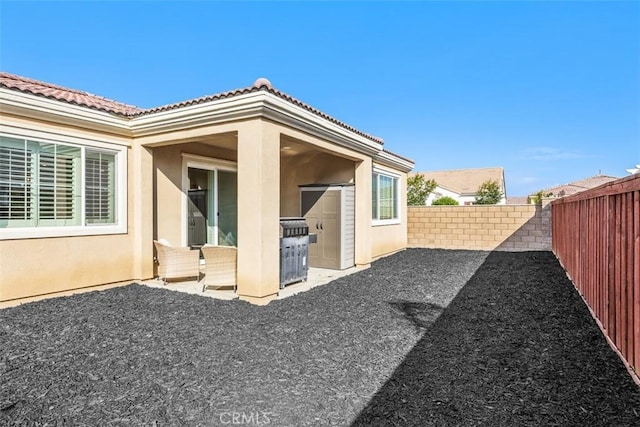 rear view of house with a fenced backyard, stucco siding, a patio area, and a tiled roof