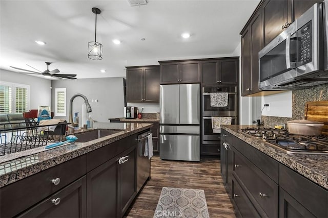 kitchen featuring appliances with stainless steel finishes, a sink, dark brown cabinets, backsplash, and dark wood-style floors