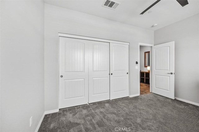 unfurnished bedroom with dark colored carpet, a closet, baseboards, and a ceiling fan