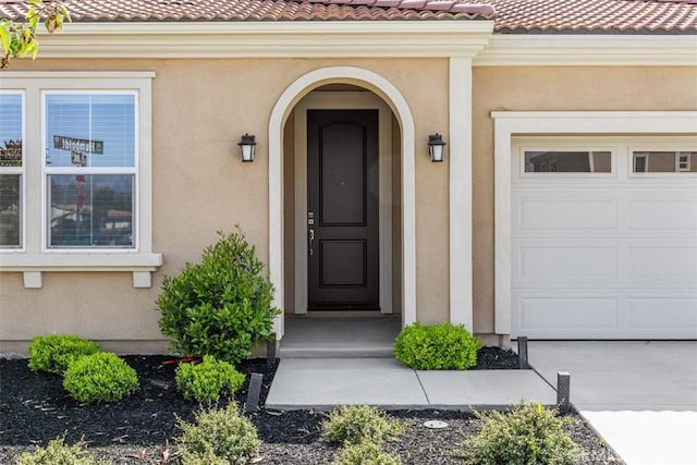 view of exterior entry with stucco siding, a tile roof, and an attached garage