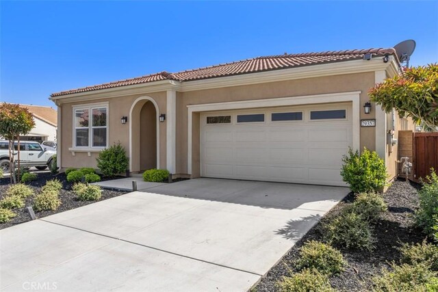 mediterranean / spanish-style home featuring an attached garage, driveway, stucco siding, and a tiled roof