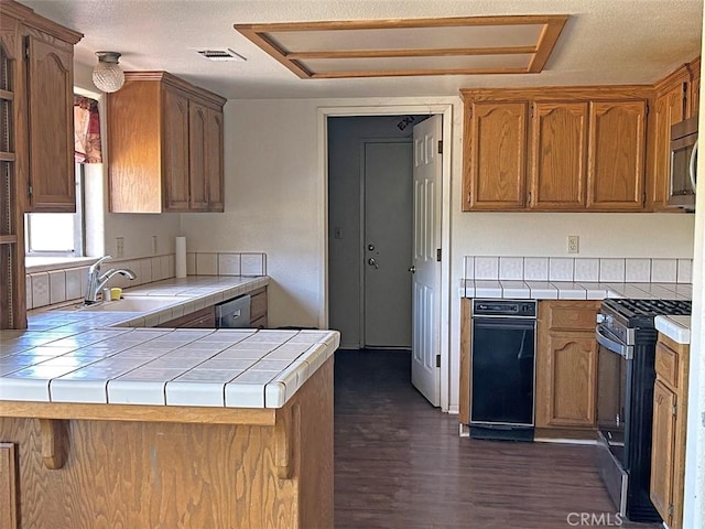 14402 Boxtree St, Lake Hughes, CA 93532 - kitchen featuring appliances with stainless steel finishes, tile counters, a peninsula, dark wood-style flooring, and brown cabinetry