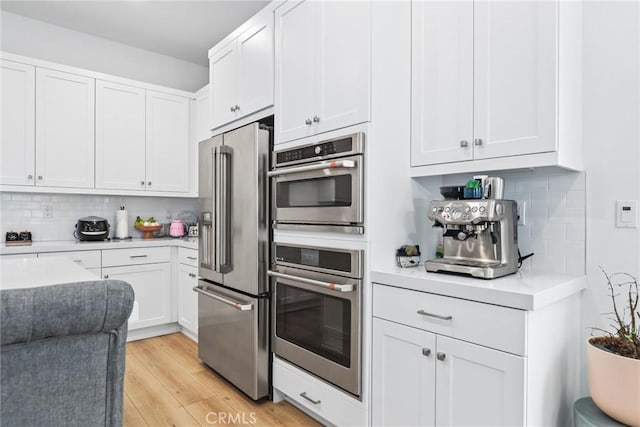 27120 Purple Sage Ct, Valencia, CA 91381 - kitchen with stainless steel appliances, light countertops, decorative backsplash, white cabinetry, and light wood-style floors