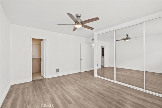 unfurnished bedroom featuring wood finished floors, ensuite bath, baseboards, and ceiling fan