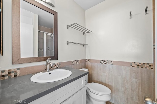 full bathroom with tile walls, a shower stall, toilet, vanity, and wainscoting