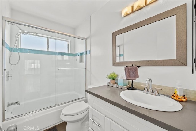 full bath with toilet, vanity, and shower / bath combination with glass door