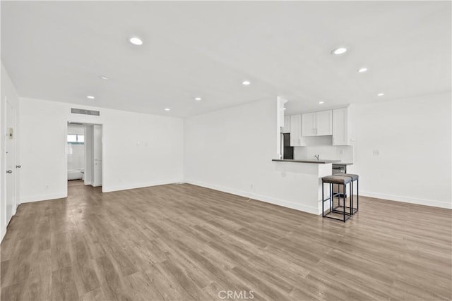 unfurnished living room featuring recessed lighting, light wood finished floors, and baseboards