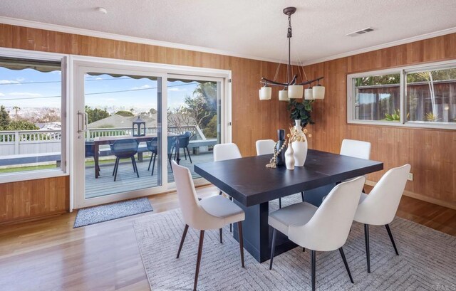 dining space featuring wood walls, light wood finished floors, crown molding, and baseboards