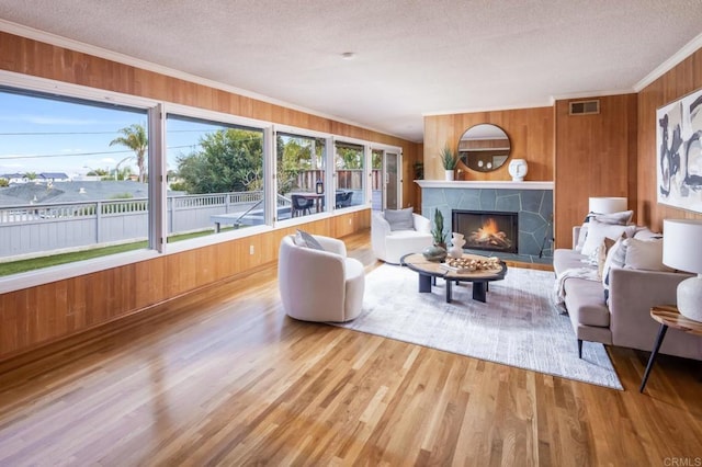 living room featuring crown molding, wood walls, a textured ceiling, wood finished floors, and a stone fireplace