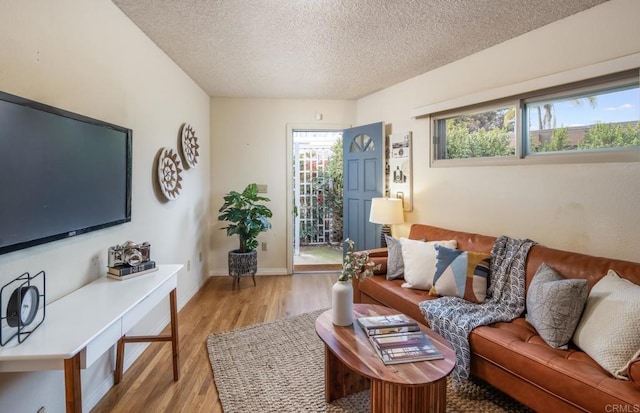 living room with a textured ceiling, light wood-style flooring, and baseboards