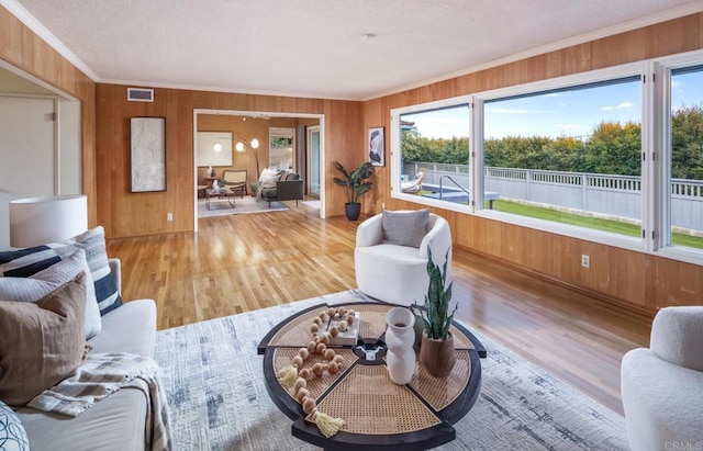 living area with crown molding, wooden walls, plenty of natural light, and wood finished floors