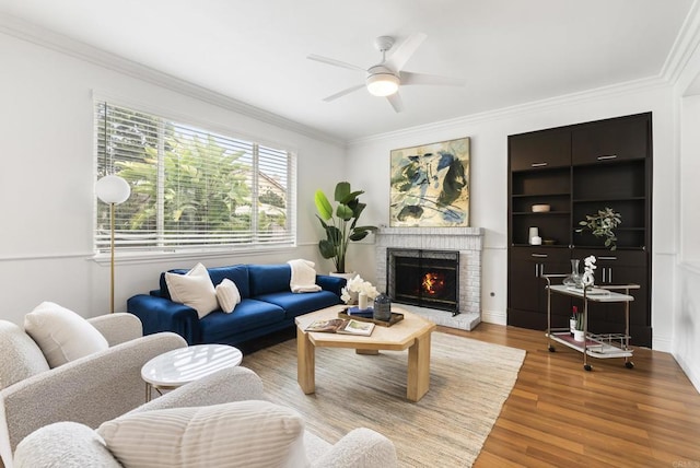 living area featuring a fireplace, a ceiling fan, ornamental molding, and wood finished floors