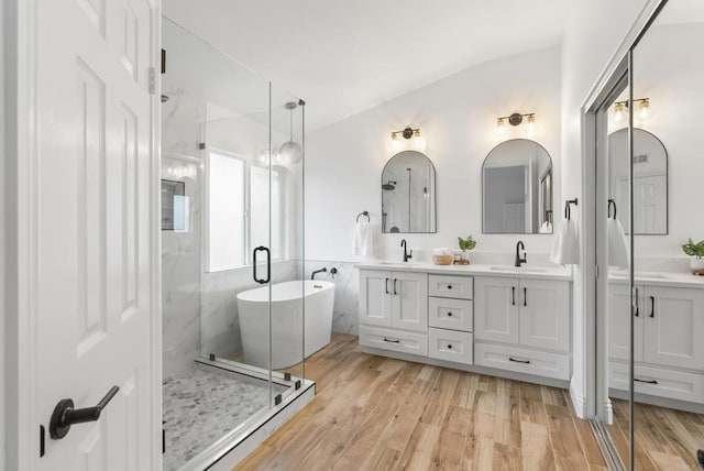 full bathroom featuring a stall shower, double vanity, wood finished floors, and vaulted ceiling