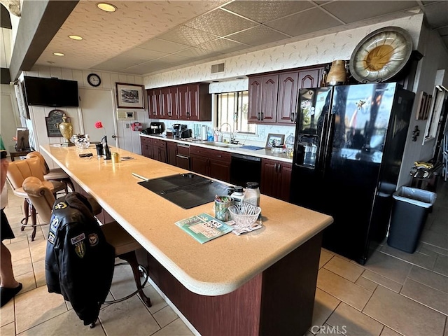 kitchen with black appliances, a sink, light countertops, dark brown cabinetry, and a drop ceiling
