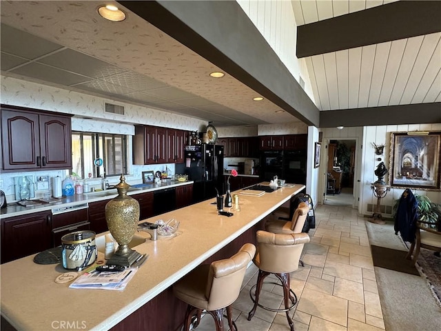 kitchen featuring black appliances, light countertops, a breakfast bar, stone tile flooring, and recessed lighting