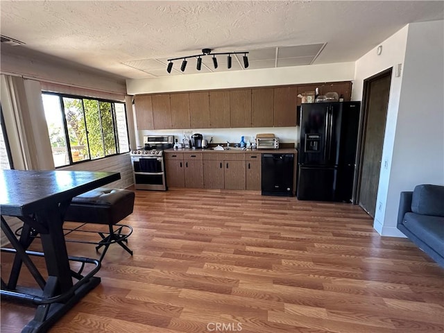 kitchen featuring black appliances, a sink, wood finished floors, a textured ceiling, and dark brown cabinetry