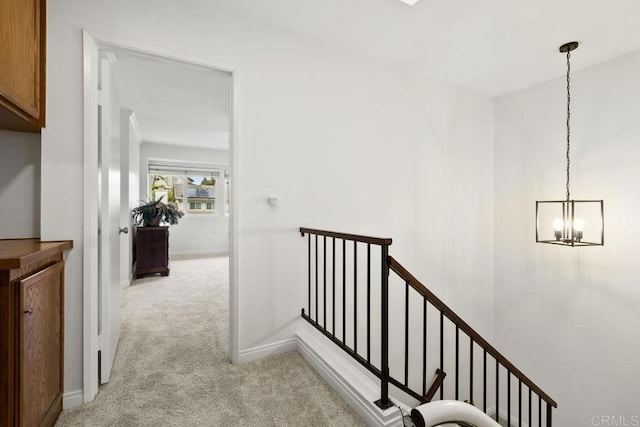 hallway featuring carpet floors, an upstairs landing, a chandelier, and baseboards
