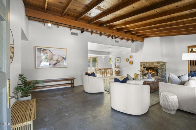 living room featuring finished concrete flooring, a stone fireplace, beam ceiling, wood ceiling, and rail lighting