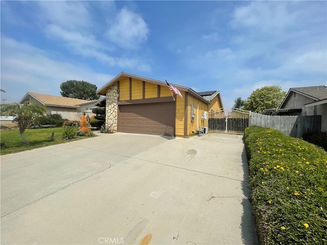 view of property exterior with concrete driveway, a gate, fence, solar panels, and a garage