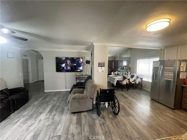 living room featuring a textured ceiling, wood finished floors, ornamental molding, baseboards, and a ceiling fan