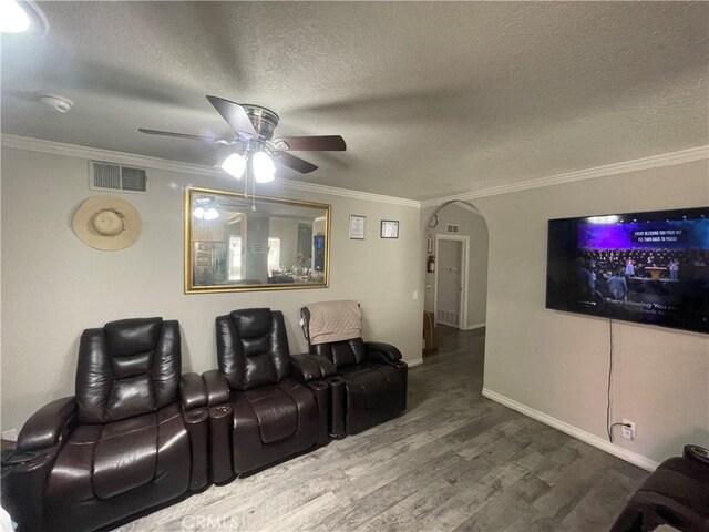 cinema room featuring ceiling fan, arched walkways, ornamental molding, wood finished floors, and a textured ceiling