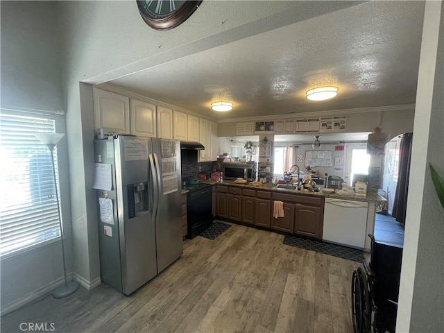 kitchen with appliances with stainless steel finishes, under cabinet range hood, a peninsula, a sink, and wood finished floors