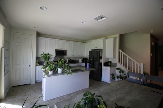 kitchen featuring black refrigerator with ice dispenser, stainless steel microwave, white cabinets, a center island with sink, and recessed lighting