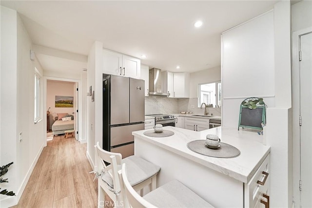 3004 Via Buena Vis Unit C, Laguna Woods, CA 92637 - kitchen with wall chimney range hood, appliances with stainless steel finishes, light wood-style flooring, white cabinetry, and a peninsula