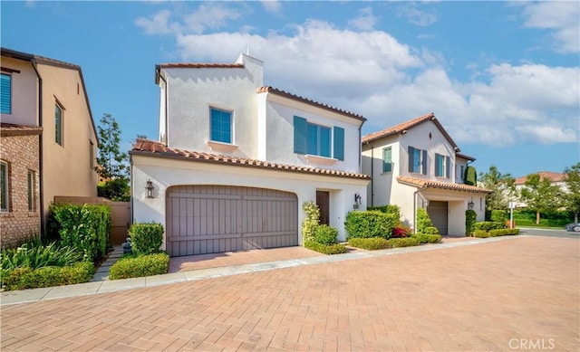 mediterranean / spanish home featuring stucco siding, a tile roof, a garage, and decorative driveway