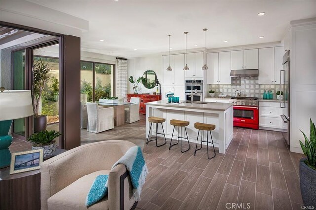 kitchen featuring premium appliances, under cabinet range hood, decorative backsplash, white cabinetry, and light countertops