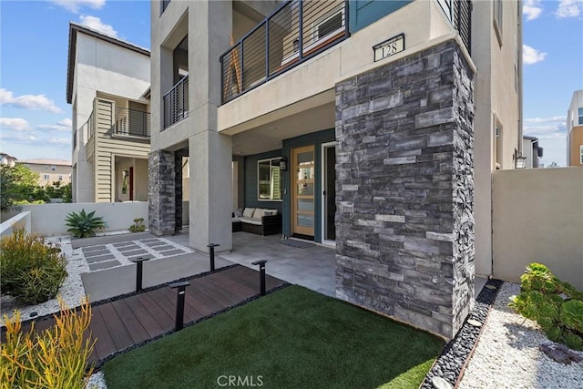rear view of house with stucco siding, stone siding, fence, and an outdoor hangout area