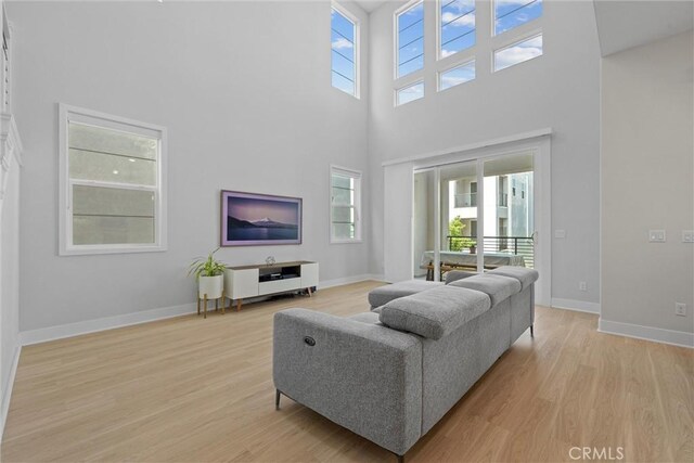 living area featuring a high ceiling, light wood finished floors, and baseboards