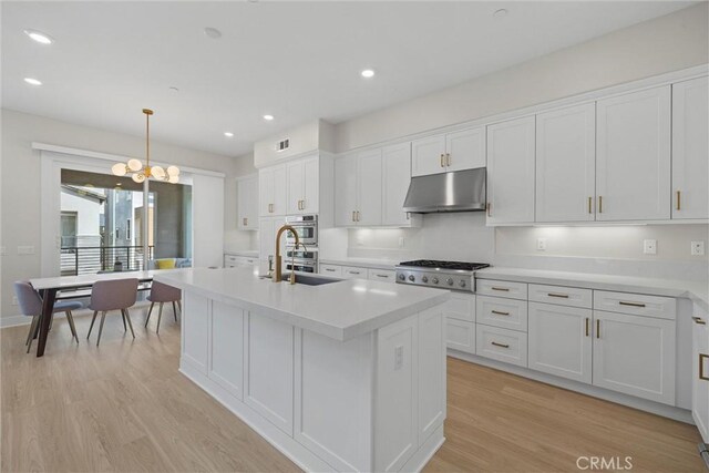 kitchen featuring under cabinet range hood, gas stovetop, white cabinetry, light countertops, and recessed lighting