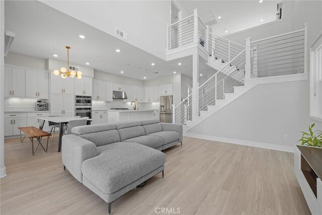 living area with stairway, recessed lighting, light wood-style floors, a chandelier, and a high ceiling