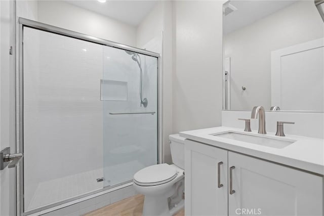 bathroom with a shower stall, toilet, wood finished floors, and vanity