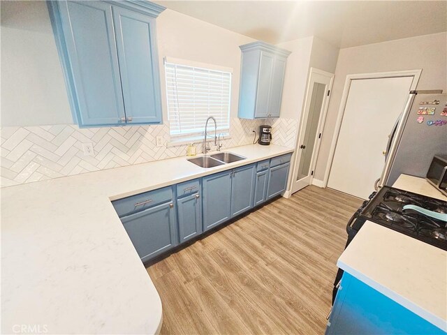kitchen featuring a sink, blue cabinetry, freestanding refrigerator, tasteful backsplash, and light countertops