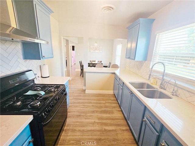 kitchen featuring gas stove, wall chimney exhaust hood, a sink, light wood-style floors, and decorative backsplash