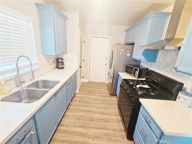 kitchen with blue cabinetry, a sink, black gas range, wall chimney exhaust hood, and backsplash