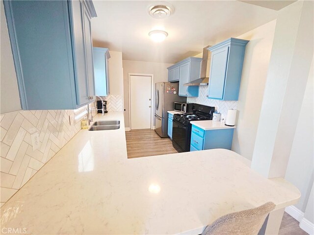 kitchen with appliances with stainless steel finishes, a sink, backsplash, blue cabinetry, and light countertops