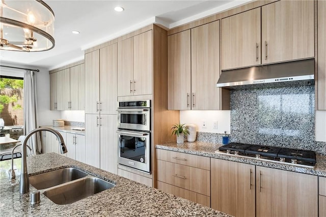kitchen with under cabinet range hood, a sink, appliances with stainless steel finishes, light brown cabinetry, and light stone counters