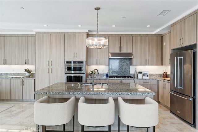 kitchen with appliances with stainless steel finishes, a breakfast bar, dark stone countertops, a kitchen island with sink, and recessed lighting