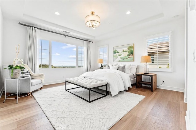 bedroom featuring a raised ceiling, light wood-style flooring, baseboards, and recessed lighting