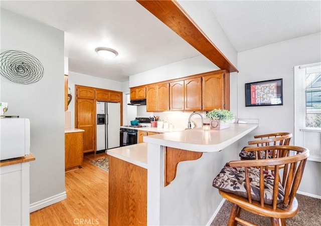 4702 Castana Ave, Lakewood, CA 90712 - kitchen with white fridge with ice dispenser, gas range oven, a peninsula, light countertops, and a kitchen breakfast bar