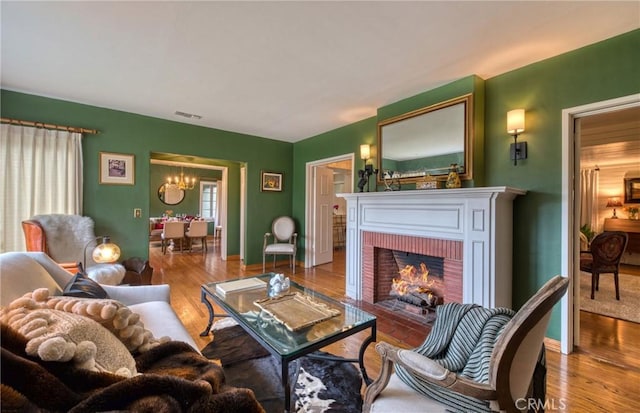 living room with a chandelier, wood finished floors, a brick fireplace, and baseboards
